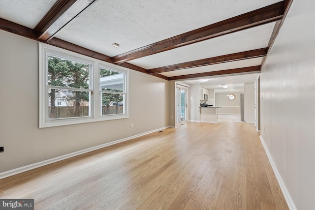 unfurnished living room with light wood-style flooring, a textured ceiling, baseboards, and beamed ceiling