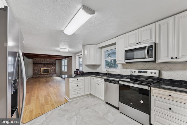 kitchen with a peninsula, white cabinets, open floor plan, appliances with stainless steel finishes, and tasteful backsplash