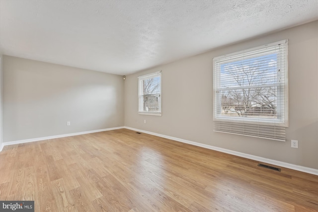 spare room with baseboards, visible vents, a textured ceiling, and light wood finished floors