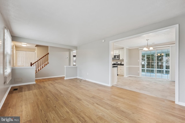 unfurnished living room with light wood-style floors, stairway, baseboards, and an inviting chandelier