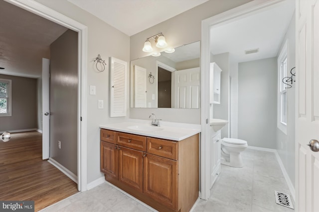 bathroom with toilet, vanity, visible vents, and baseboards