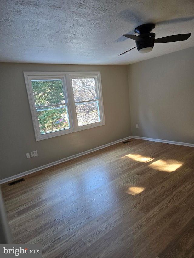 empty room featuring a textured ceiling, wood finished floors, visible vents, and baseboards