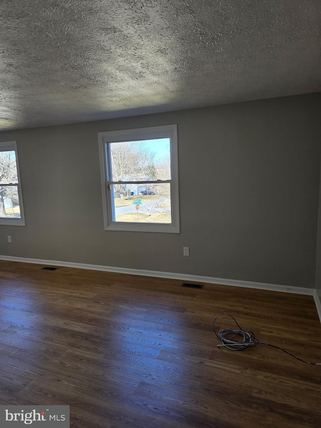 unfurnished room with dark wood-style floors, baseboards, visible vents, and a textured ceiling