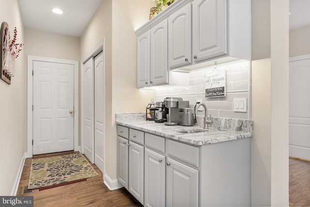 kitchen with light stone counters, backsplash, a sink, and wood finished floors