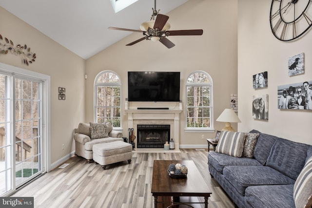 living area with ceiling fan, high vaulted ceiling, a fireplace with flush hearth, baseboards, and light wood-type flooring