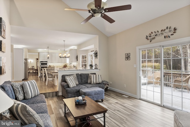 living area featuring ceiling fan with notable chandelier, high vaulted ceiling, light wood-style flooring, and baseboards