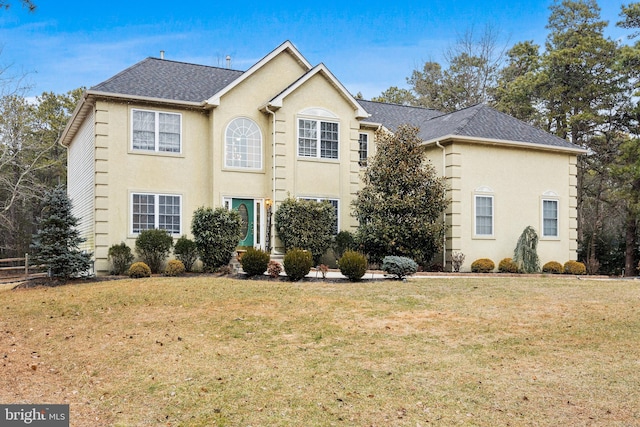 view of front of home with a shingled roof, a front yard, and stucco siding