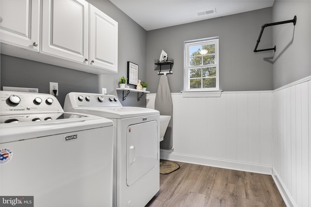 laundry room featuring cabinet space, visible vents, wainscoting, separate washer and dryer, and light wood-type flooring