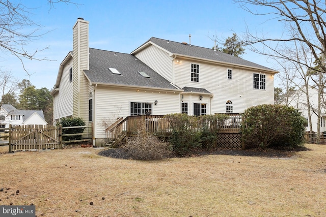 back of house with a deck, roof with shingles, a chimney, and fence