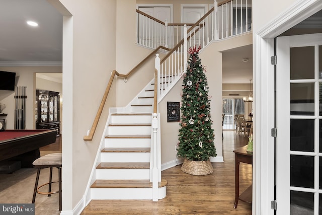 stairs featuring pool table, a high ceiling, wood finished floors, baseboards, and crown molding