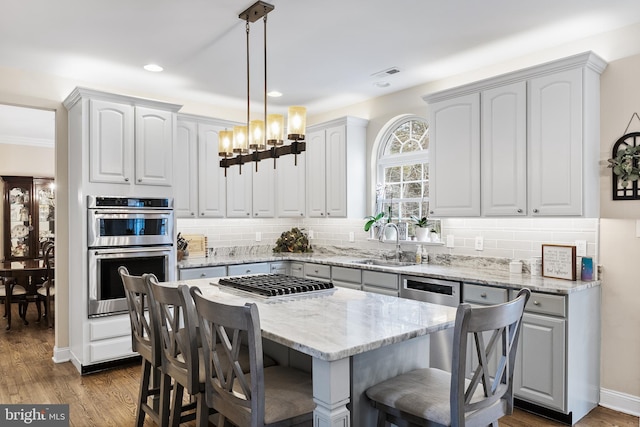 kitchen with tasteful backsplash, light stone countertops, stainless steel appliances, a kitchen bar, and a sink