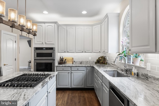 kitchen with dark wood-style floors, stainless steel appliances, tasteful backsplash, a sink, and light stone countertops