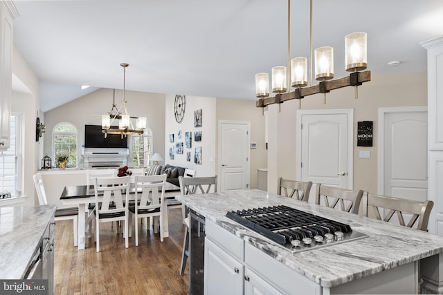 kitchen with a breakfast bar area, wood finished floors, vaulted ceiling, stainless steel gas stovetop, and white cabinetry