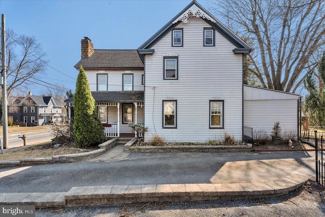 victorian house with a shingled roof, covered porch, a chimney, and fence