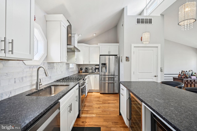 kitchen featuring a sink, visible vents, white cabinets, appliances with stainless steel finishes, and wall chimney exhaust hood