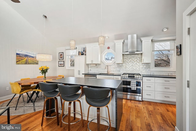 kitchen featuring dark countertops, white cabinets, a sink, wall chimney range hood, and double oven range