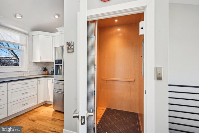 kitchen with dark countertops, light wood-style flooring, white cabinets, and backsplash