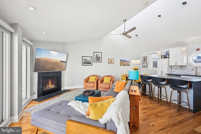 living room featuring lofted ceiling, a fireplace with flush hearth, a ceiling fan, light wood-type flooring, and baseboards