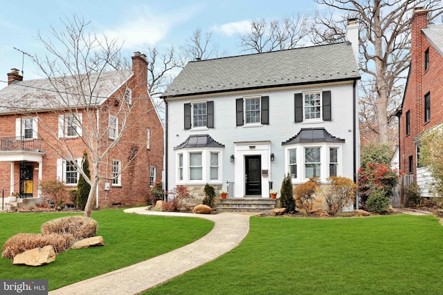 view of front facade featuring a front yard, brick siding, a chimney, and a high end roof