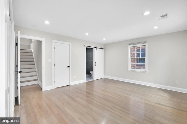 unfurnished bedroom featuring light wood finished floors, a barn door, visible vents, and recessed lighting