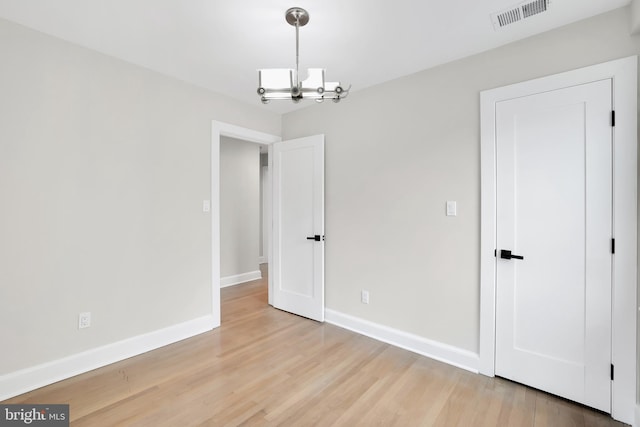 interior space with a chandelier, wood finished floors, visible vents, and baseboards