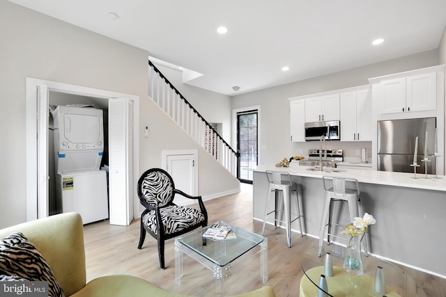 living room featuring recessed lighting, baseboards, stairs, light wood-style floors, and stacked washer and clothes dryer