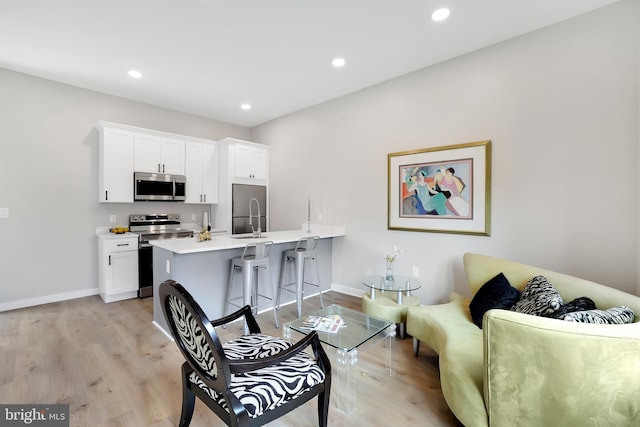 interior space featuring a breakfast bar, light countertops, appliances with stainless steel finishes, light wood-style floors, and white cabinetry