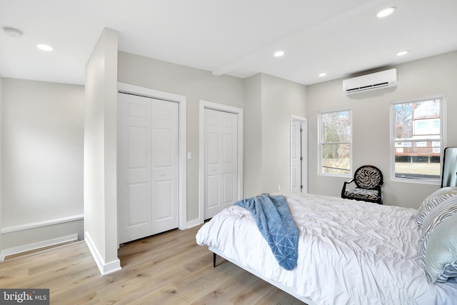 bedroom with a wall unit AC, recessed lighting, baseboards, light wood finished floors, and two closets