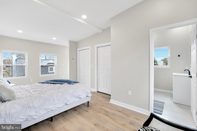 bedroom with light wood-style floors, multiple windows, baseboards, and two closets