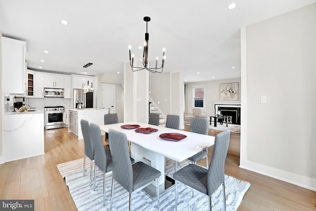 dining space featuring stairway, light wood-type flooring, a fireplace, a notable chandelier, and recessed lighting