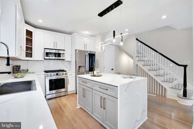 kitchen with white cabinets, a kitchen island, glass insert cabinets, decorative light fixtures, and stainless steel appliances