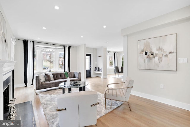 living room featuring a fireplace with flush hearth, recessed lighting, baseboards, and light wood finished floors