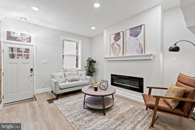 living area featuring a glass covered fireplace, recessed lighting, baseboards, and light wood-style floors