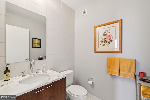 half bathroom with toilet, visible vents, vanity, and tile walls