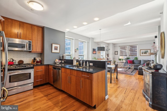 kitchen with brown cabinets, appliances with stainless steel finishes, open floor plan, a sink, and a peninsula