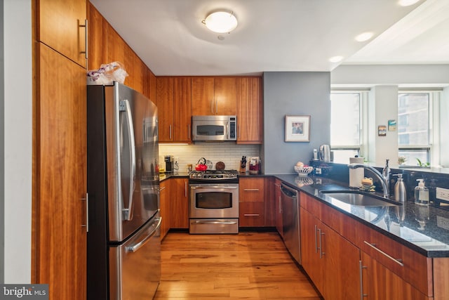 kitchen with stainless steel appliances, brown cabinetry, a sink, and light wood-style flooring