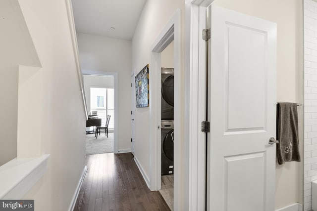 hall with stacked washer / drying machine, baseboards, and dark wood-type flooring