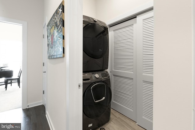 clothes washing area featuring baseboards, stacked washer and clothes dryer, wood finished floors, and laundry area