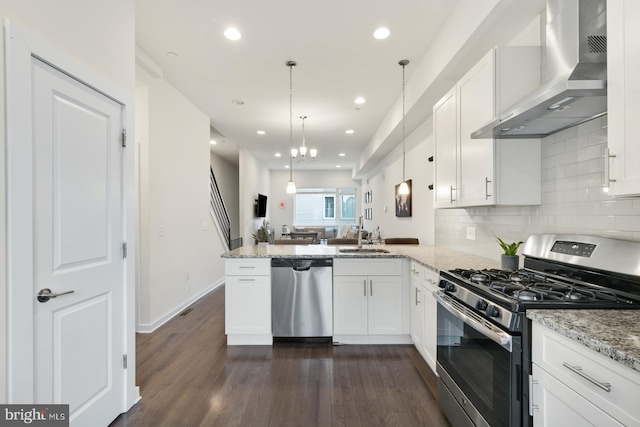 kitchen with a peninsula, dark wood-type flooring, appliances with stainless steel finishes, white cabinetry, and wall chimney range hood