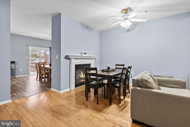 dining room featuring a ceiling fan, a glass covered fireplace, baseboards, and light wood finished floors