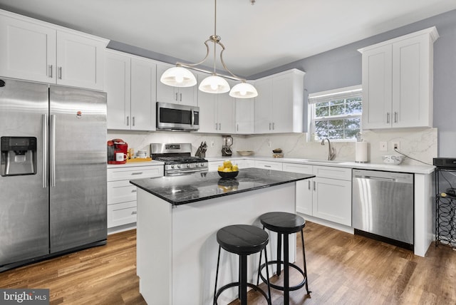 kitchen featuring hanging light fixtures, appliances with stainless steel finishes, white cabinets, a kitchen island, and a sink