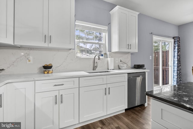 kitchen featuring tasteful backsplash, white cabinets, dark wood-style floors, stainless steel dishwasher, and a sink