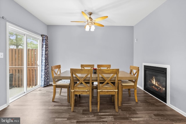 dining room featuring dark wood-type flooring, a glass covered fireplace, ceiling fan, and baseboards