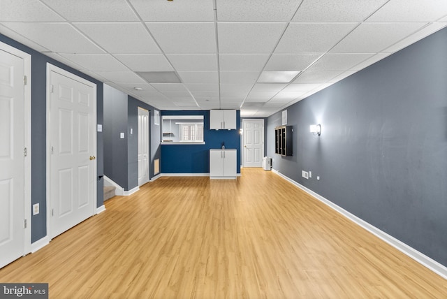 unfurnished living room featuring light wood-type flooring, a paneled ceiling, and baseboards