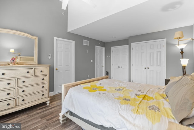 bedroom with baseboards, visible vents, dark wood finished floors, and two closets