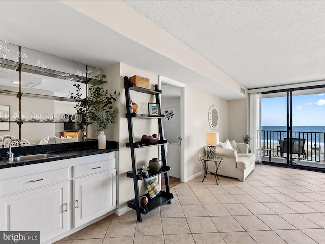 bar featuring white cabinetry, a water view, sink, light tile patterned floors, and a textured ceiling