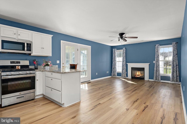 kitchen with light wood-type flooring, appliances with stainless steel finishes, a peninsula, white cabinets, and a healthy amount of sunlight