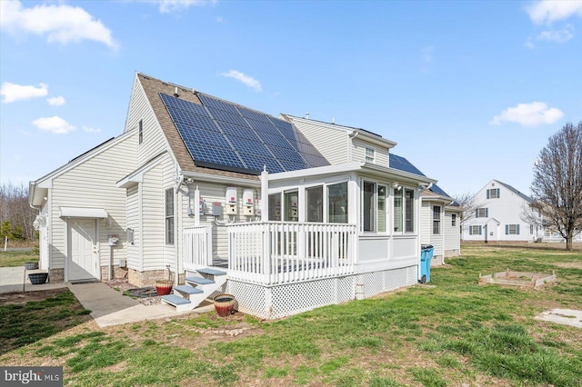 back of house featuring roof mounted solar panels, a lawn, a sunroom, and roof with shingles