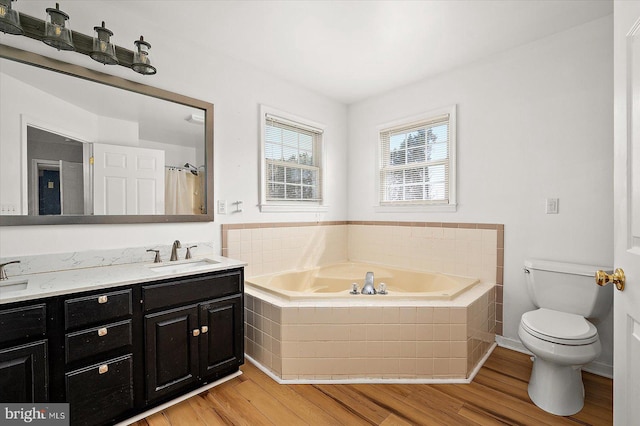 bathroom featuring toilet, a sink, wood finished floors, double vanity, and a bath