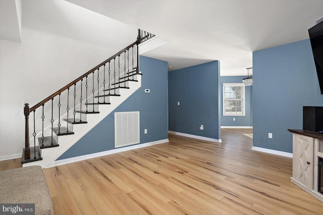 unfurnished living room with visible vents, stairway, light wood-type flooring, and baseboards